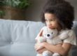 young girl sitting alone on couch hugging a stuffed animal can help adults in recognizing autism in girls