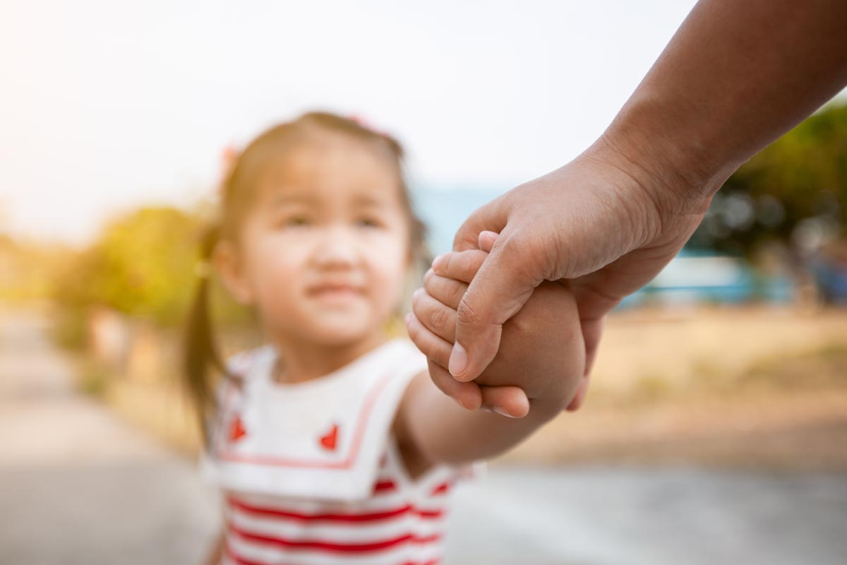 Identifying Non-Verbal Autism in Children small female child being taken by the hand by caring adult who is identifying non verbal autism in children