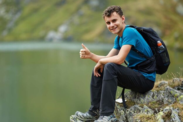 5 Autism-Friendly Activities adolescent male child sitting by lake giving thumbs up as he participates in one of 5 autism friendly activities