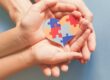 two pairs of hands holding a heart made of multi-colored puzzle pieces observing autism awareness day