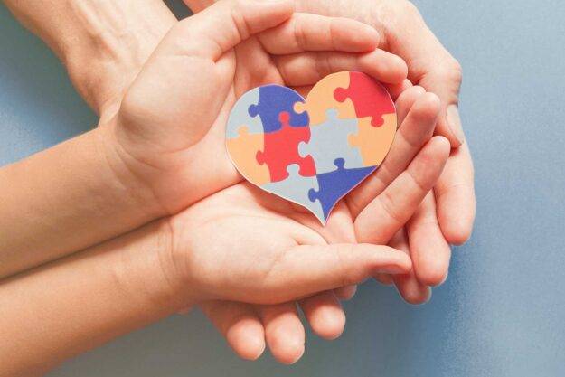 Observing Autism Awareness Day two pairs of hands holding a heart made of multi-colored puzzle pieces observing autism awareness day