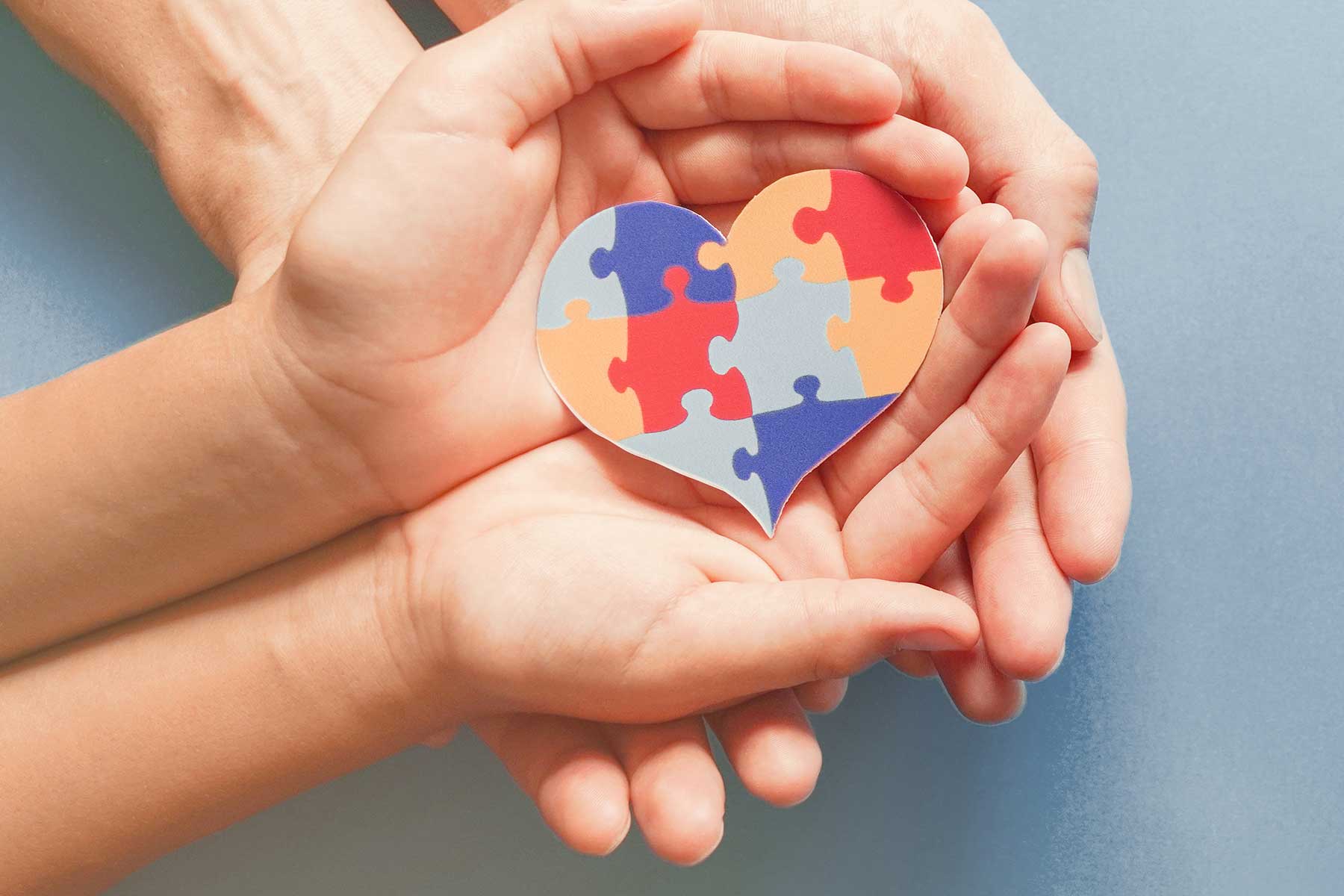 two pairs of hands holding a heart made of multi-colored puzzle pieces observing autism awareness day